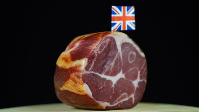 Delicious smoked tenderloin with small flag of United Kingdom, piece of meat rotating on balck background.