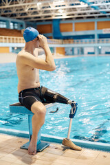 Athletic amputee adjusts his swimming goggles while preparing for a swim at indoor pool.