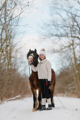 hübsches Welsh Mountain Pony mit jungem Mädchen im Winter, Reitpferd mit schöner Blesse im...