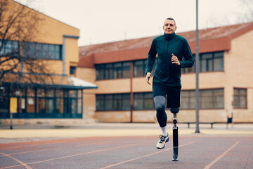 Male runner with prosthetic leg running during practice on outdoor sports field.