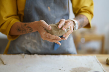 Female potter artist molding raw clay. Closeup of woman ceramist in dirty apron prepare for shaping pottery. Craftswoman hands work with earthenware. Art studio production and craftsmanship therapy