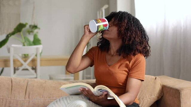 Dominican woman with curly hair reading a book and drinking coffee
