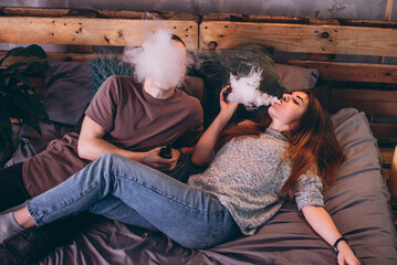 Stylish couple vaping in bed. Two people use the electronic cigarette