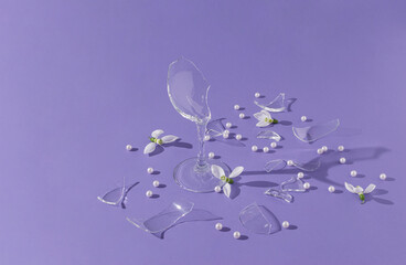 Creative composition made with pieces of broken wine glass,  white pearls and snowdrop flowers on purple background. Spring party concept. Sunshine shadows.