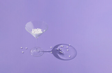Martini glass with white pearls on purple background. Minimal party concept. Sunshine shadows.