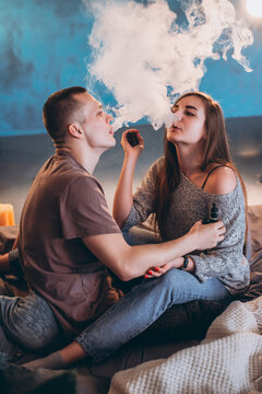 Man and young woman smoking e-cigarettes and exhaling smoke