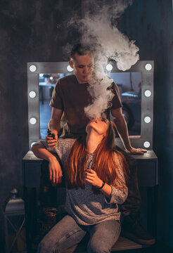 Man and young woman smoking e-cigarettes and exhaling smoke