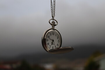 Vintage pocket watch hanging against cloudy sky
