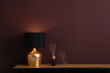 Wooden table with decor and lamp near brown wall in room, space for text