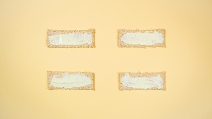 Four rectangular whole grain crisps are spread with white sauce and prepared for sandwiches.