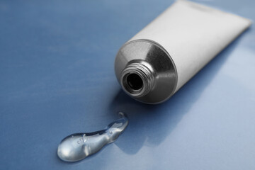Open white tube with ointment on blue background, closeup