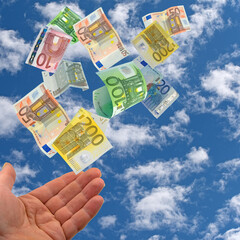 Aufgehaltene Hand und Geldscheine vor Himmel mit Wolken