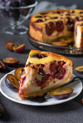 French curd pie with plums and cinnamon, ready to eat on a plate on a gray table