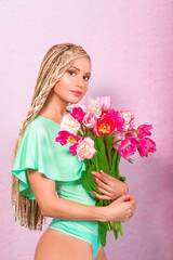 attractive blonde young woman with african braids with tulips on pink background