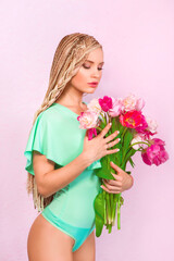 attractive blonde young woman with african braids with tulips on pink background