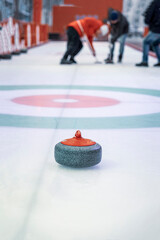 Granite projectile for curling on ice against background of playing athletes, selective focus
