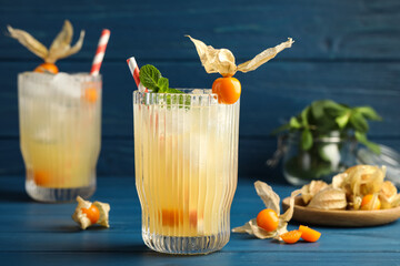Refreshing cocktail decorated with physalis fruit on blue wooden table