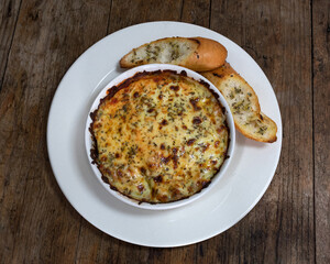 Lasaña mixta con salsa bolognesa, queso mozzarella, pollo, champiñon, orégano, y pan de ajo en plato blanco sobre un fondo de madera