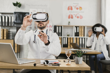 Caucasian male doctor and african american nurse working at medical cabinet in VR headset. Revolutionizing in medical industry with advanced technology.