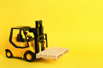 Toy forklift with wooden pallet on yellow background, space for text