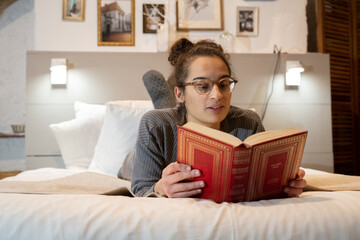 Lecture d'un livre par une jeune femme allongée sur un lit