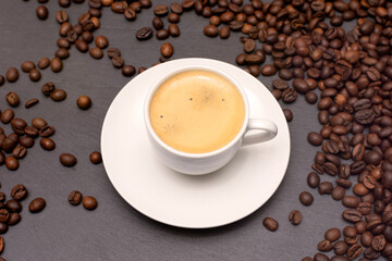 white cup with espresso coffee on a saucer with coffee beans on a dark background