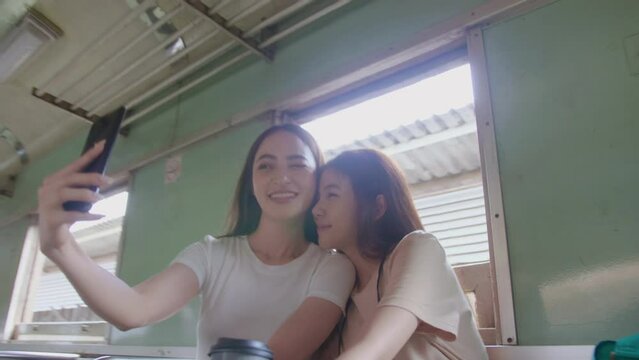 Young Beautiful cozy woman lgbts couples take a photo on the train. Gimbal orbit shot. Asian woman sweetness taking a photo together while traveling in Thailand on summer vacation.