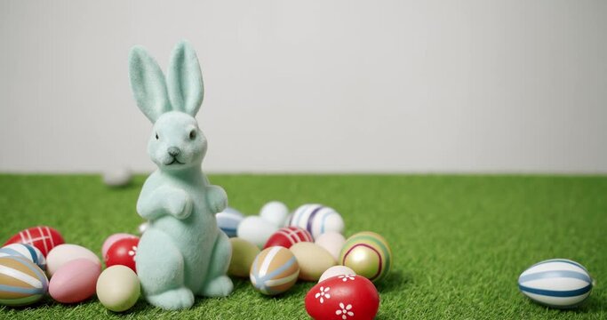Rabbit toy on a white background of green grass with many colored eggs. Place for Text. Cute fluffy rabbit, Lovely Animal concept. Happy Easter day