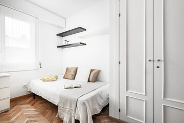 Fototapeta na wymiar Bedroom with small white bed, herringbone parquet and white wooden built-in wardrobe in vacation rental apartment