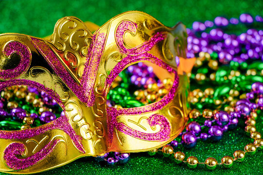 Carnival mask and colorful beads on green shiny background. Mardi Gras concept. Fat Tuesday symbol.