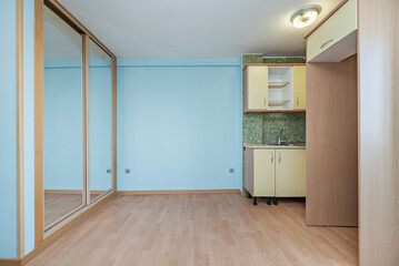 Studio with a corner kitchen with a green tiled wall and the rest of the walls painted light blue and in front of the kitchen a built-in wardrobe with sliding glass doors