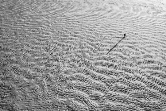 Aerial view of tiny lone skier on frozen snow covered textured lake - Powered by Adobe