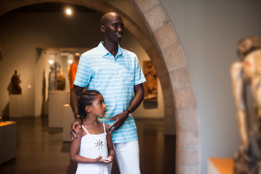 African American man and his daughter visiting exposition of museum with exhibits of medieval art