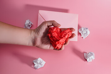 hand of aggressive and frustrated man squeezing heart out of crumpled paper. envelope with lumps of paper scattered. Letter to a Loved One on Valentine's Day