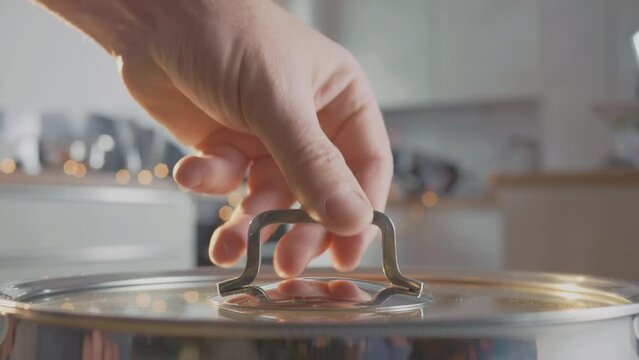 Close up shot of white smoke and steam over the pot closed with glass cover by male hand.
