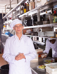 Fototapeta na wymiar Confident chef of restaurant posing in kitchen on background with working employees