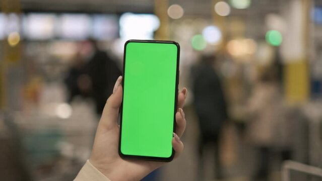 young woman hand using smart phone with green screen in the market. close-up chroma key mock up hypermarket. woman holding phone with green screen in the mall. shopping in the mall