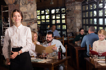 Professional waitress greeting customers at table in rustic restaurant. High quality photo
