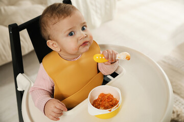 Cute little baby wearing bib while eating at home