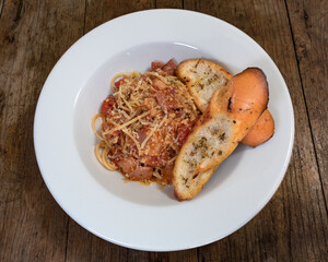 Pasta con salsa roja, tomate, cebolla roja, tocineta y queso parmesano en un plato blanco sobre un fondo de madera