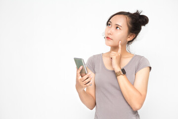 Beautiful Asian woman wearing grey casual shirt holding smartphone on white background and copy space.  Cute Asian woman is thinking and chatting about something for social media concept