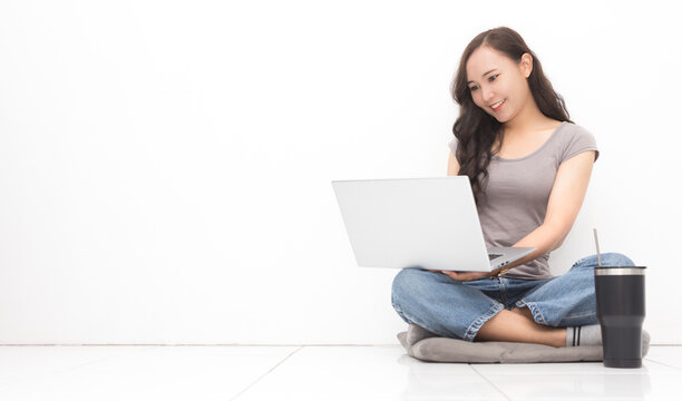 Beautiful Asian woman wearing grey casual shirt using laptop on white background and copy space.  Cute Asian woman sitting on the floor room relaxing for work from home concept