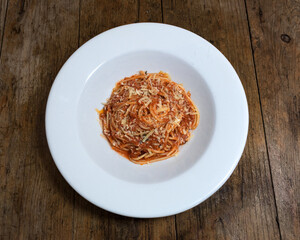 Pasta con salsa bolognesa y queso parmesano en un plato blanco sobre un fondo de madera