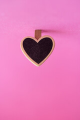 detalle de clip en forma de corazón de madera negra de pizarrón con fondo rosa fucsia y desenfoque