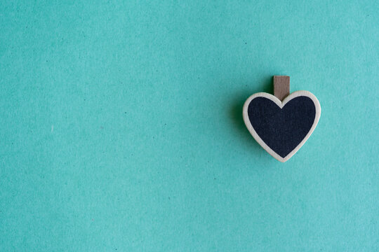 detalle de clip en forma de corazón de madera negra de pizarrón con fondo de papel verde turquesa