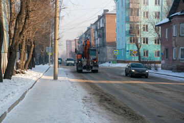Orange excavator moving along the city winter road.