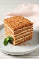 Fototapeta na wymiar Slice of delicious layered honey cake with mint served on white wooden table, closeup