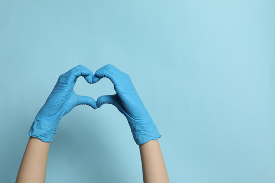 Doctor in medical gloves making heart with hands on light blue background, closeup. Space for text