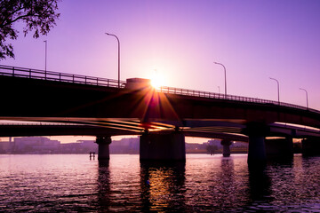 朝日に照らされた海の上の橋と通行中のトラックのシルエット