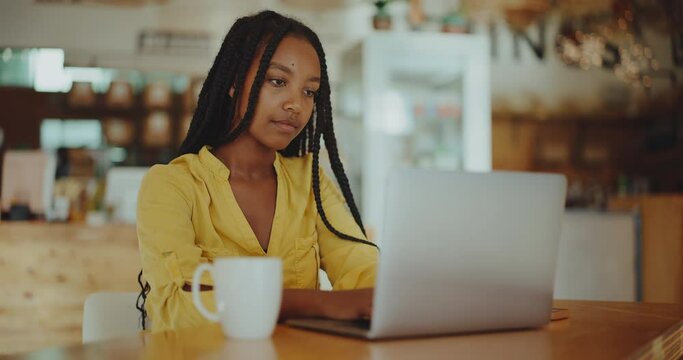 Successful young black woman working remotely in coffee shop on her laptop, success and diversity, future of remote work, young successful african american entrepreneur
